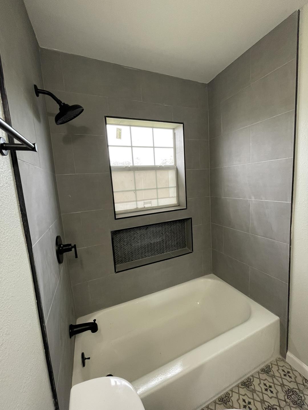 Bathroom remodel with large-format gray tile, tub surround, and matte black fixtures