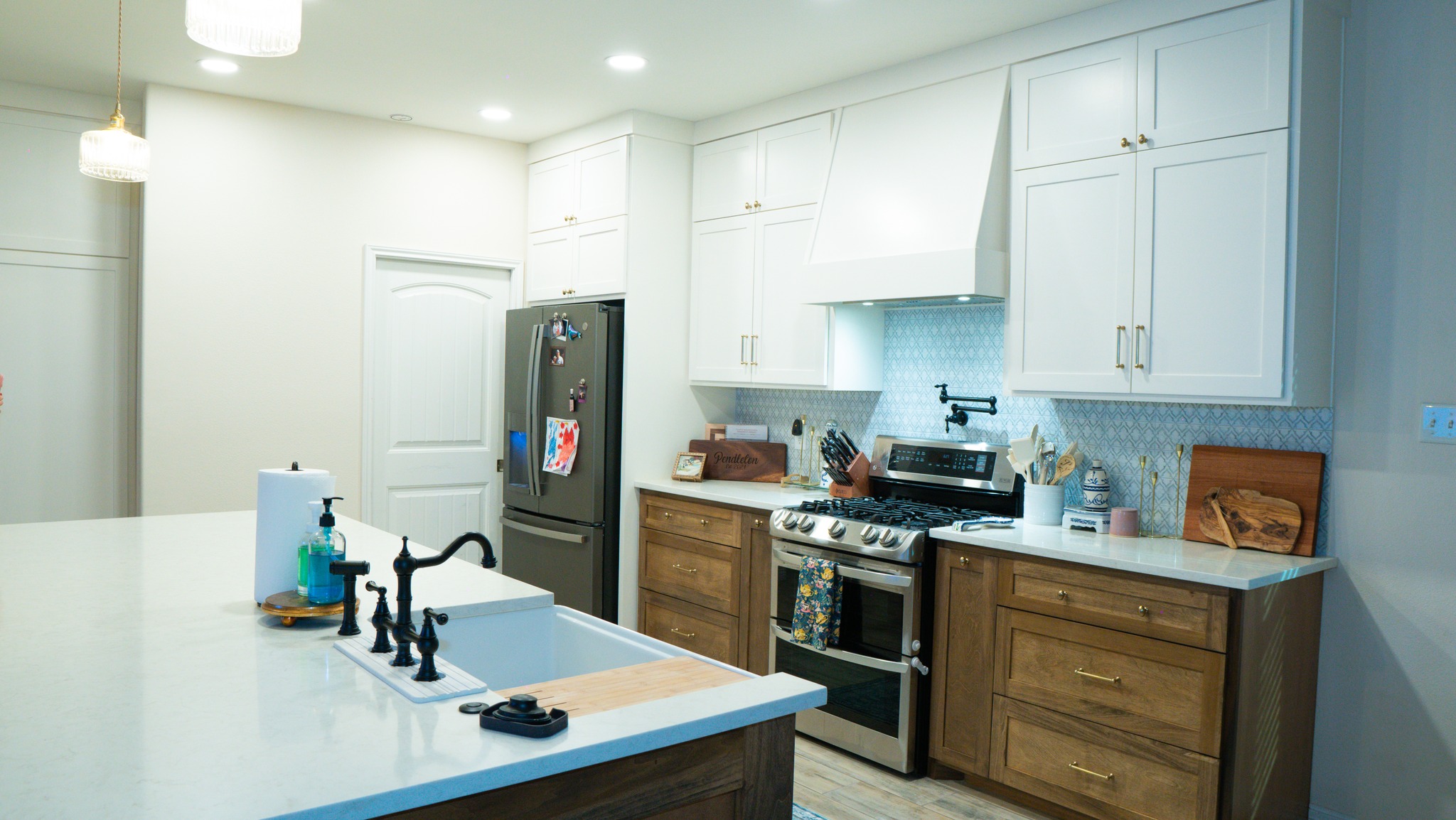 Kitchen with white upper cabinets, wood lower cabinets, quartz counters, and blue tile backsplash