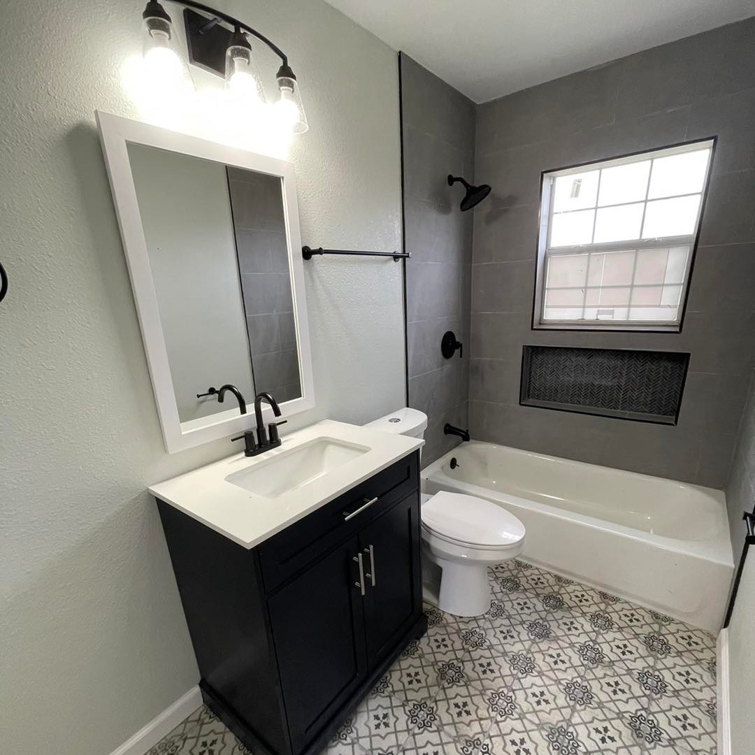 Bathroom with dark vanity, white countertop, patterned floor tile, and gray tile tub surround