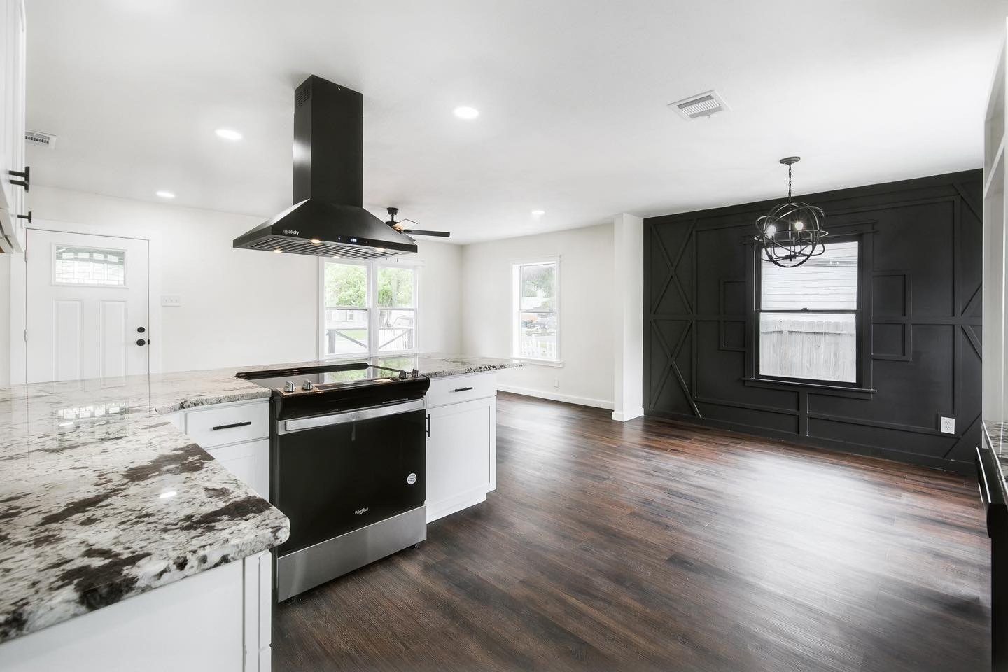 Open kitchen and living remodel with black accent wall, black range hood, and granite counters