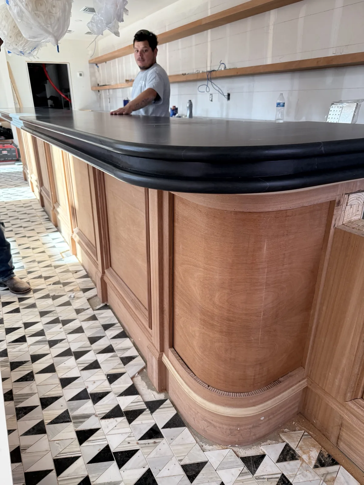 Custom curved mahogany bar millwork in progress with honed stone countertop